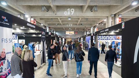 People walking and talking in a well-lit exhibition corridor lined with ski and outdoor equipment brands at ProWinter