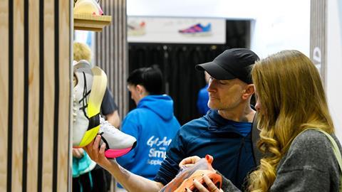 A man and woman compare running shoes at a display wall featuring bright performance footwear.
