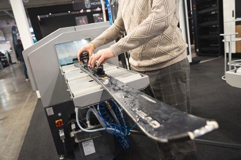 Person demonstrating a ski service machine, placing a ski into the device to show tuning or maintenance equipment at the trade fair.