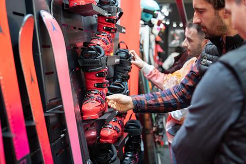 Visitors examining red ski boots displayed on a wall, discussing product details at the Atomic booth.