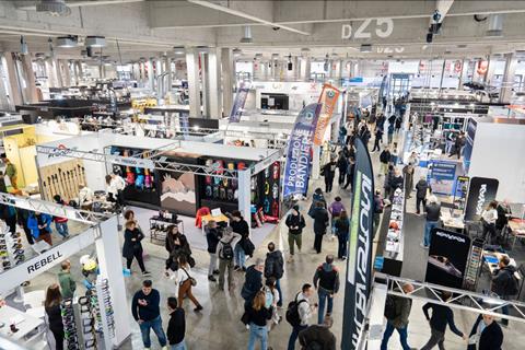 Wide view of a large trade fair hall with multiple exhibition booths, banners, and visitors walking through the aisles at ProWinter