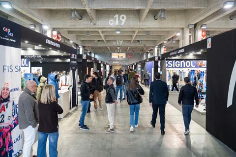 People walking and talking in a well-lit exhibition corridor lined with ski and outdoor equipment brands at ProWinter