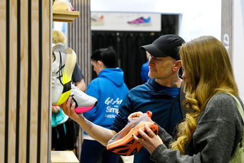 A man and woman compare running shoes at a display wall featuring bright performance footwear.