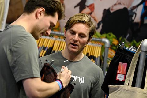 Two men discuss a pair of sports shorts at a trade fair booth at IRX showcasing athletic apparel.